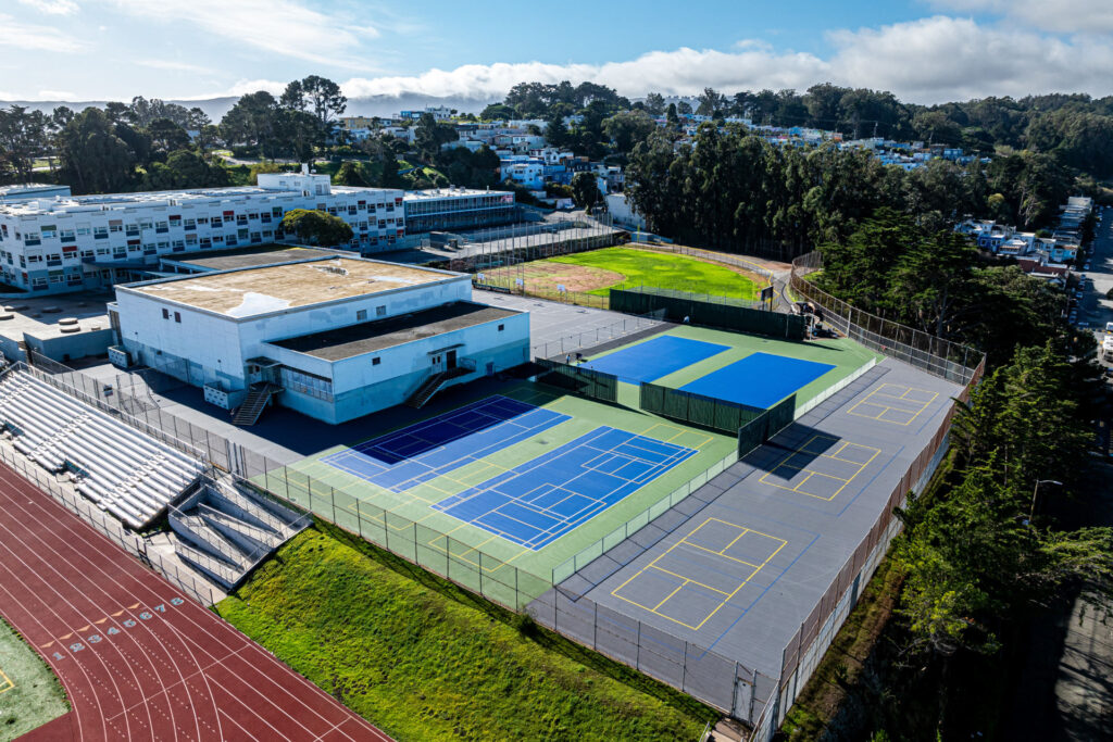 Tennis courts at Phillip and Sala Burton Academic High School in San Francisco with embedded pickleball layouts. The tennis courts were refurbished using the slipsheet overlay system and surfaced with Plexipave acrylic resurfacer and color in dark blue and medium green