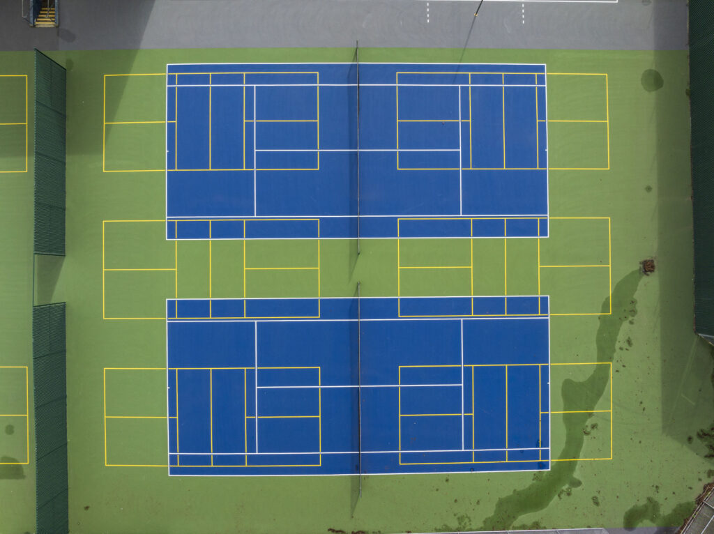 Tennis courts at Phillip and Sala Burton Academic High School in San Francisco with embedded pickleball layouts. The tennis courts were refurbished using the slipsheet overlay system and surfaced with Plexipave acrylic resurfacer and color in dark blue and medium green