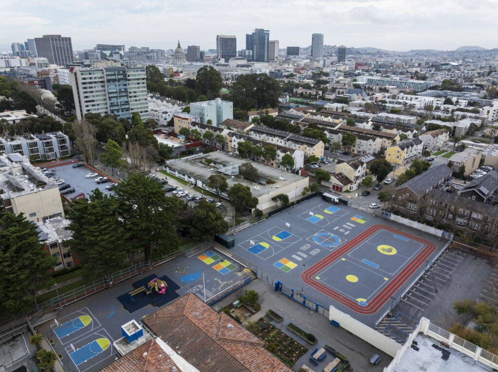 Aerial city view of the playground at Rosa Parks Elementary School in San Francisco. The playground has various multi-use and multi-color playground layouts and was refurbished using the slipsheet overlay system. Some of the layouts include running track, hopscotch, foursquare, basketball courts and general game courts all done using Laykold Advantage acrylic resurfacer paint